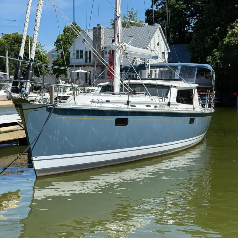 The Image of 2024 Tartan 455 sailboat docked in a marina, surrounded by trees and buildings. - 0