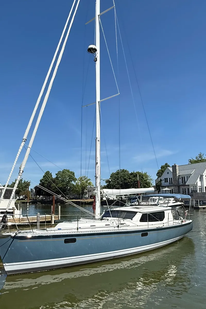Slide: The Image of 2024 Tartan 455 sailboat docked in a marina, clear blue sky, waterfront homes in background. - 23