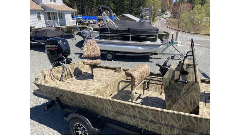 Slide: The Image of 2025 Lowe Roughneck RX1760 Pathfinder boat with camo design, parked outdoors near other boats. - 8