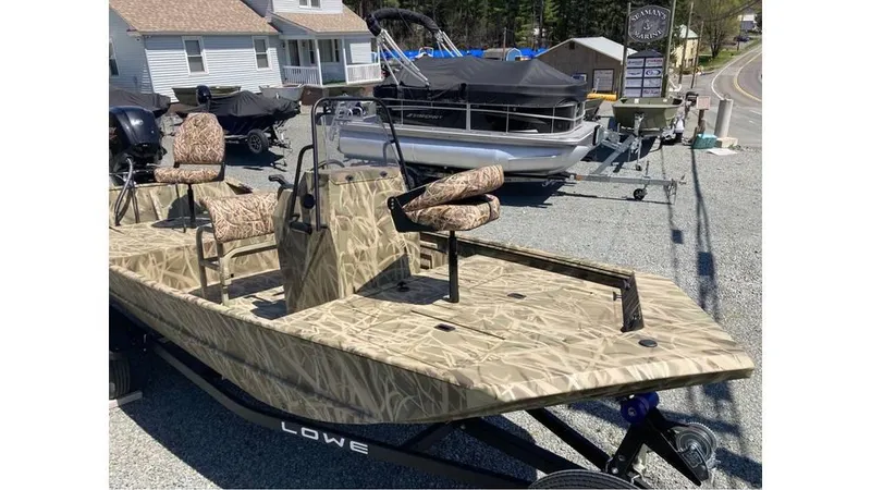 Slide: The Image of 2025 Lowe Roughneck RX1760 Pathfinder boat with camouflage design, parked outdoors. - 9