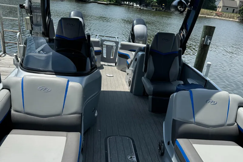 Slide: The Image of 2021 Manitou 25 XT SRS pontoon boat interior with seating, docked by a lake. - 13