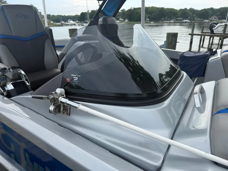 Slide: The Image of 2021 Manitou 25 XT SRS boat dashboard with windshield, docked by a serene lake. - 16