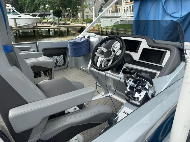 Slide: The Image of 2021 Manitou 25 XT SRS boat interior with modern steering and controls, docked by waterfront homes. - 3