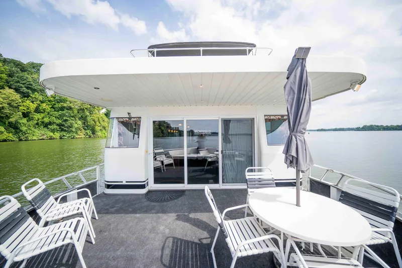 Slide: The Image of 2008 Monticello houseboat deck with chairs, table, and umbrella on a serene lake. - 15