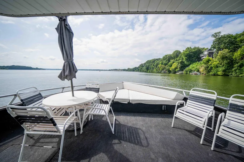 Slide: The Image of 2008 Monticello Houseboat deck with chairs, table, and umbrella overlooking serene lake and lush greenery. - 29
