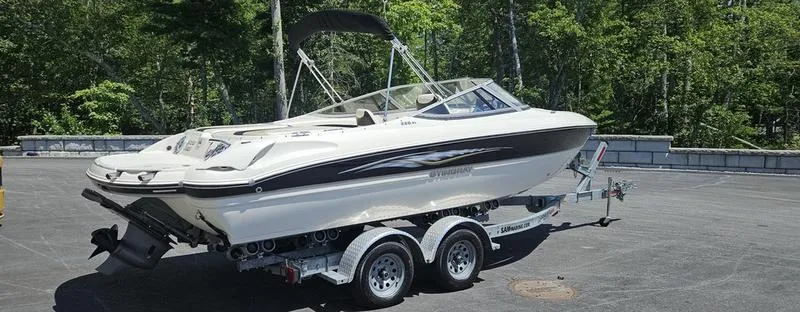 Slide: The Image of 2016 Stingray 225RX boat on trailer, parked outdoors with lush green trees in background. - 6