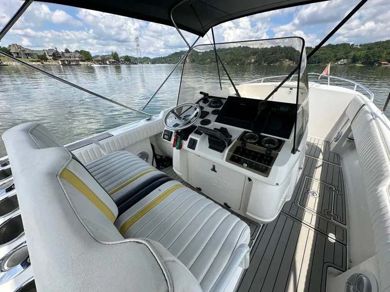 Slide: The Image of 2002 Intrepid 323 Cuddy boat interior with steering console, white seating, and scenic lake view. - 15