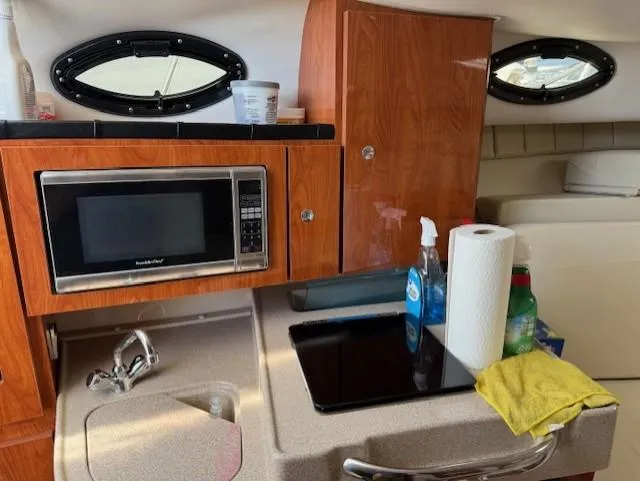 Slide: The Image of 2015 Wellcraft 290 Coastal boat interior with kitchenette, microwave, sink, and cleaning supplies. - 16