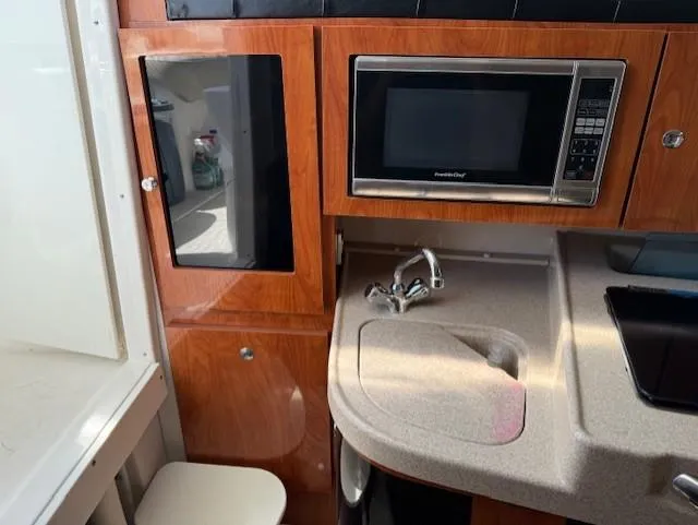 Slide: The Image of 2015 Wellcraft 290 Coastal boat interior with microwave, sink, and wooden cabinetry. - 18