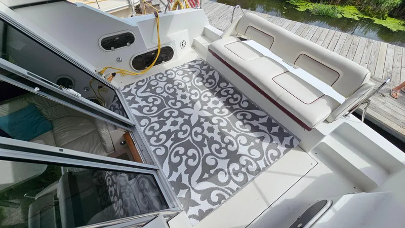 Slide: The Image of 1989 Carver 38 Santego boat deck with patterned rug and cushioned seating by a dock. - 5