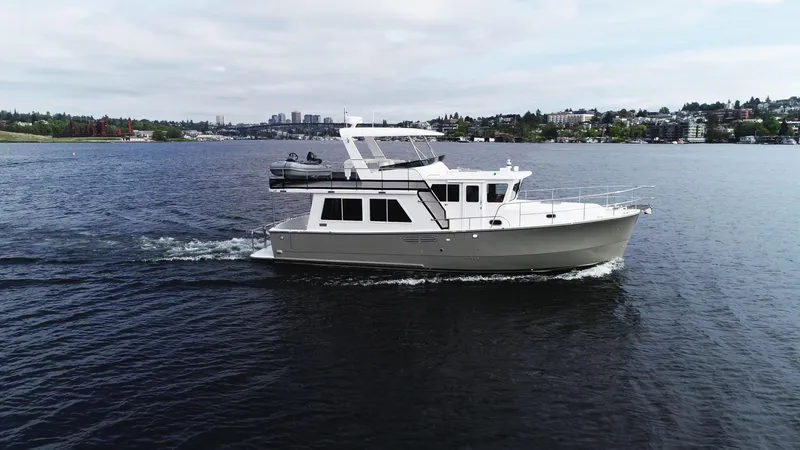 Slide: The Image of 2025 Helmsman Trawlers 43E Pilothouse cruising on a calm lake with cityscape background. - 1