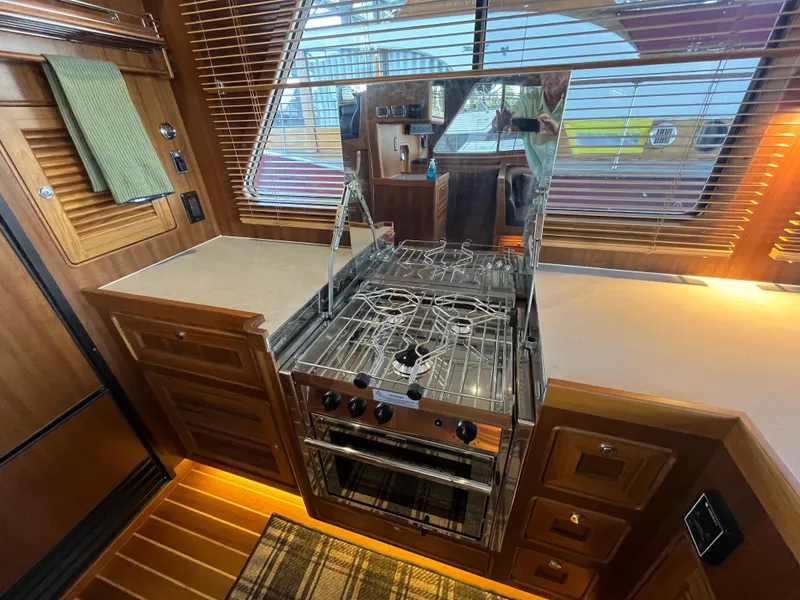 Slide: The Image of Helmsman Trawlers 43E PILOTHOUSE 2025 kitchen with stove, wooden cabinetry, and blinds. - 10