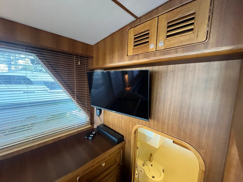Slide: The Image of Interior of 2025 Helmsman Trawlers 43E Pilothouse with TV, wooden cabinetry, and window blinds. - 5