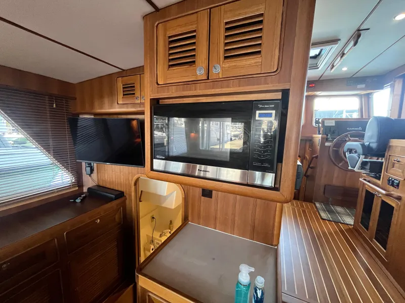 Slide: The Image of 2025 Helmsman Trawlers 43E PILOTHOUSE interior with microwave, TV, and wooden cabinetry. - 7