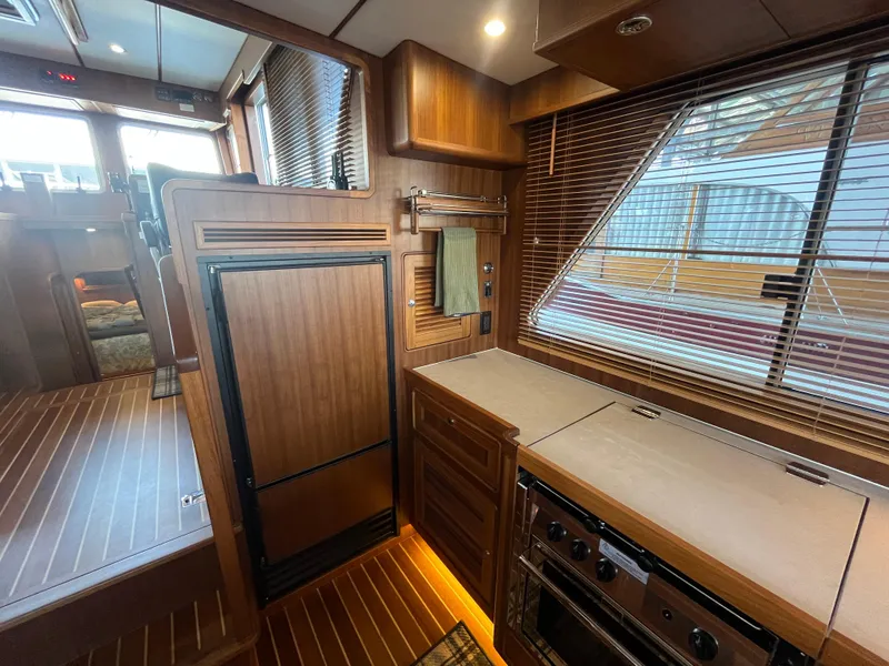 Slide: The Image of 2025 Helmsman Trawlers 43E PILOTHOUSE interior with wood finish and modern kitchen amenities. - 8