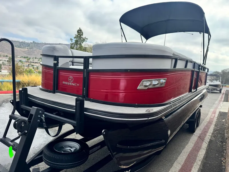 Slide: The Image of 2023 Regency 250 DL3 pontoon boat with red exterior and canopy on trailer. - 3