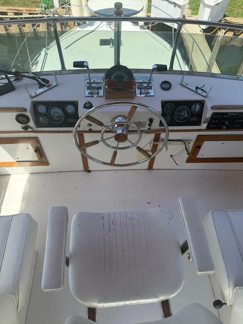 Slide: The Image of 1985 Marinette 32 Sedan helm with steering wheel and gauges, featuring white seating. - 14
