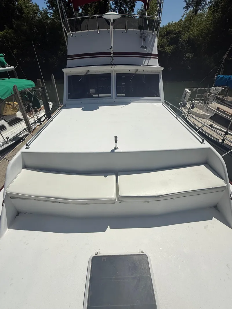 Slide: The Image of 1985 Marinette 32 Sedan boat with spacious deck and seating, docked near lush greenery. - 6