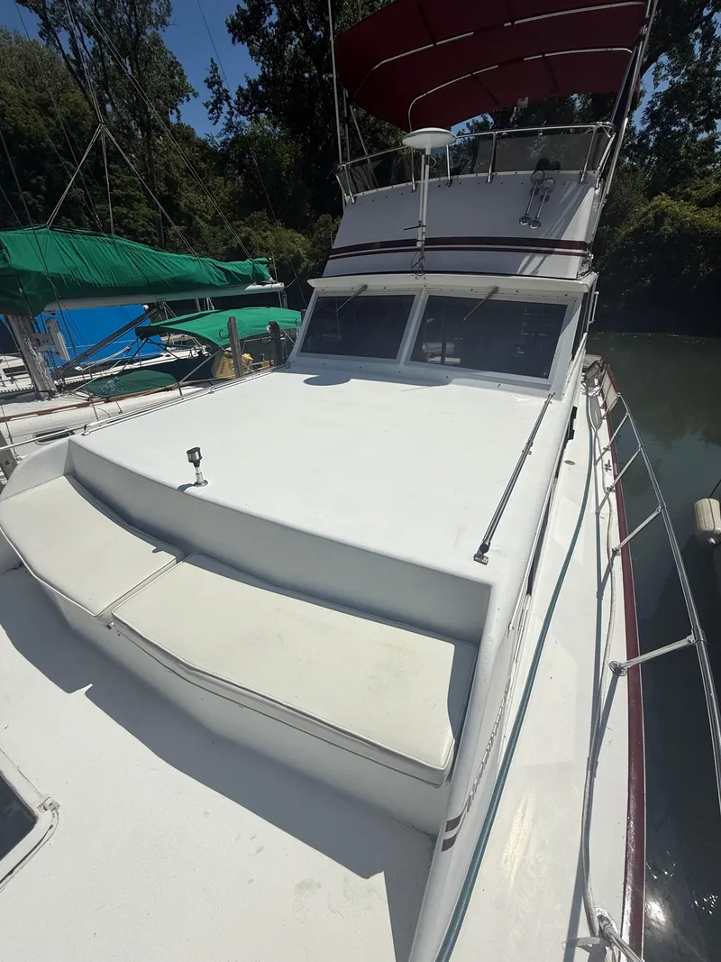 Slide: The Image of 1985 Marinette 32 Sedan boat with white deck and red canopy, docked near trees. - 8