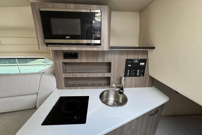 Slide: The Image of 2023 Regal 26 XO boat interior kitchen with microwave, sink, and induction cooktop. - 21