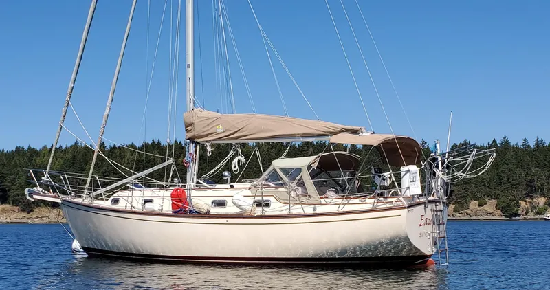 The Image of 1994 Island Packet 35 sailboat anchored on calm water with forested shoreline. - 0