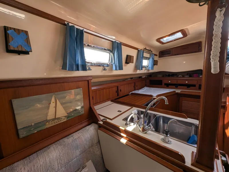 Slide: The Image of Interior of a 1994 Island Packet 35 sailboat, featuring a cozy kitchen area with wooden cabinetry. - 29
