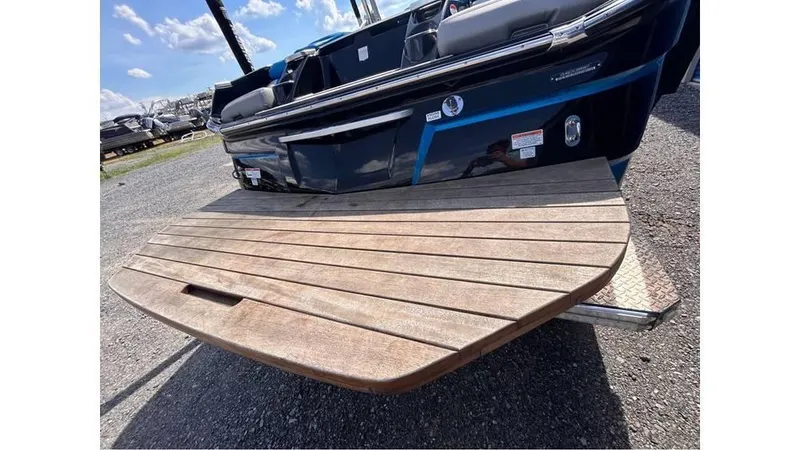 Slide: The Image of 2017 MasterCraft X23 boat with wooden swim platform, parked on gravel under a blue sky. - 22