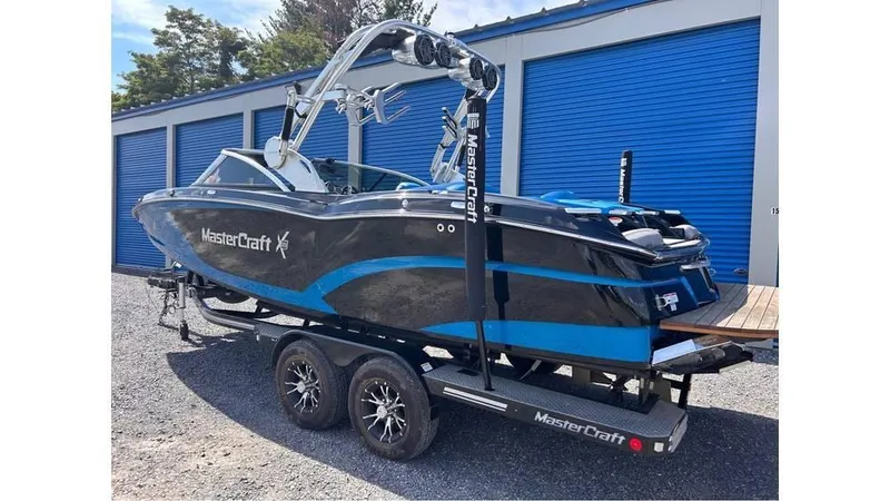 Slide: The Image of 2017 MasterCraft X23 boat on trailer, blue and black, parked near storage units. - 5