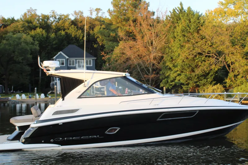The Image of 2015 Regal 35 Sport Coupe boat on a serene lake with lush trees. - 11