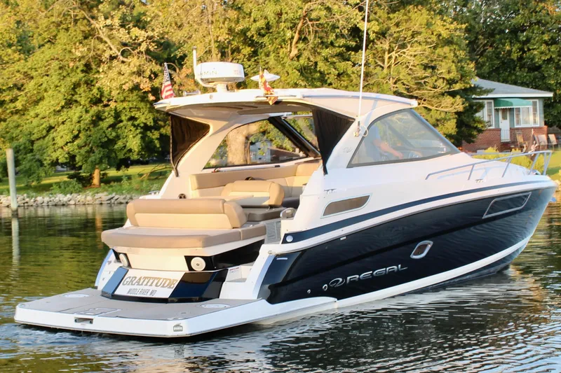 Slide: The Image of 2015 Regal 35 Sport Coupe yacht cruising on a serene lake with lush greenery. - 13