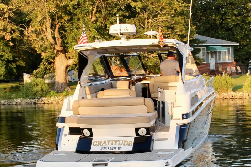 Slide: The Image of 2015 Regal 35 Sport Coupe boat cruising on a serene river near a lush, tree-lined shore. - 14