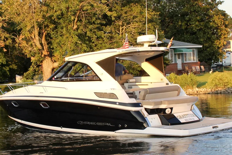 Slide: The Image of 2015 Regal 35 Sport Coupe yacht cruising on a serene lake near a house. - 17