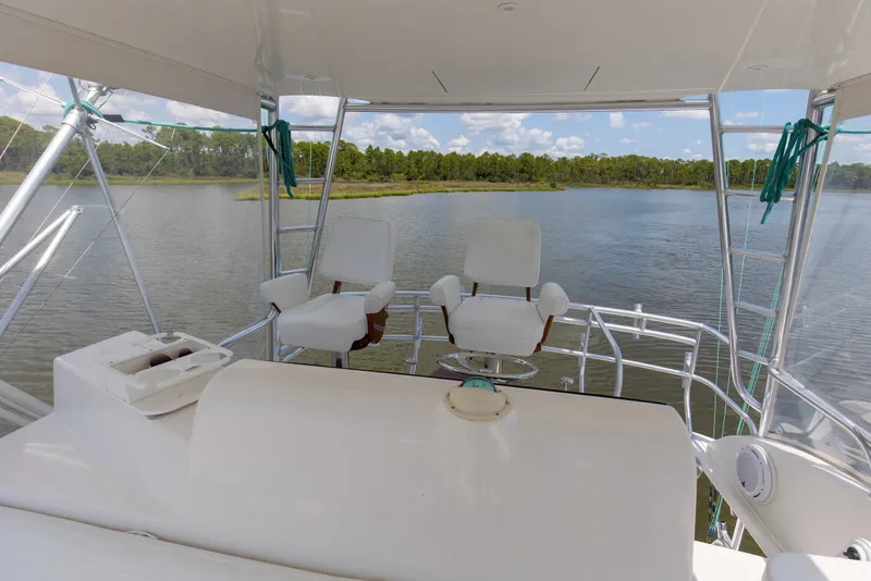 Slide: The Image of 2005 Cabo 40 Flybridge yacht interior with helm chairs overlooking serene water and lush greenery. - 77