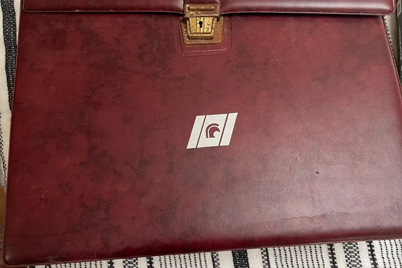 Slide: The Image of Red leather briefcase with a gold latch and logo, on a striped surface. - 49