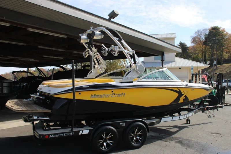 Slide: The Image of 2013 MasterCraft X-2 boat in yellow and black on a trailer, parked outdoors. - 18