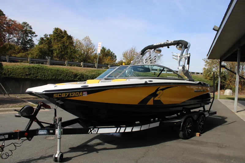 Slide: The Image of 2013 MasterCraft X-2 boat in yellow and black on a trailer, parked outdoors. - 24