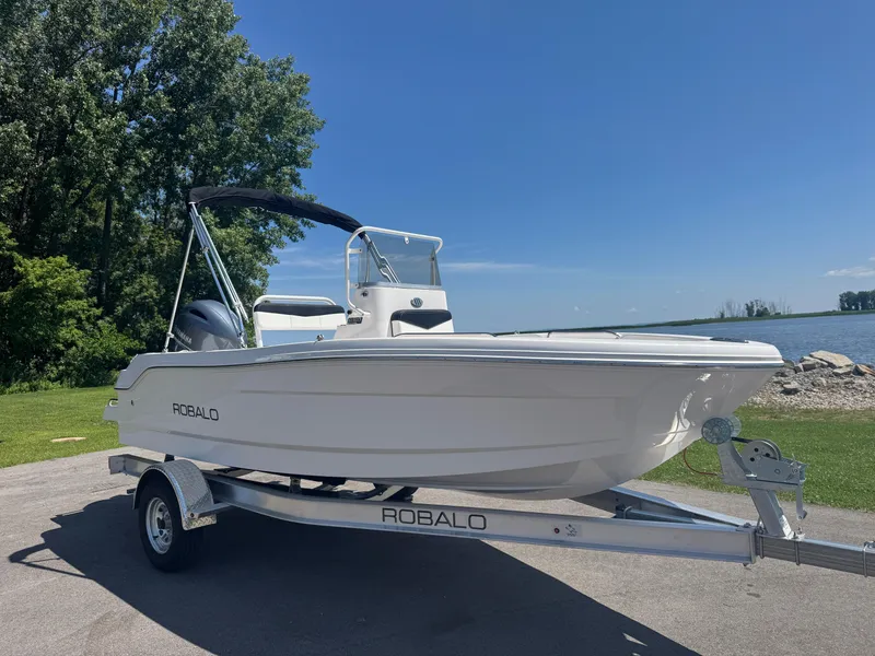 Slide: The Image of 2025 Robalo R160 Center Console boat on trailer by a lake under clear blue sky. - 1