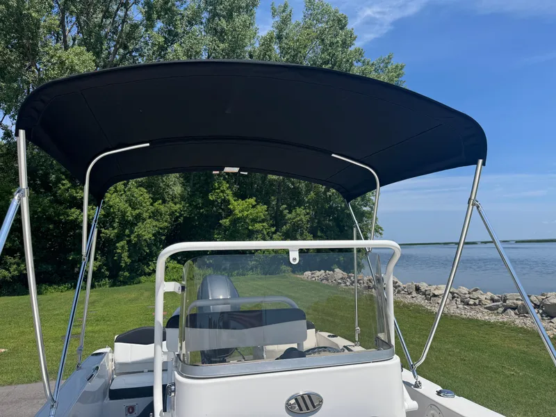 Slide: The Image of 2025 Robalo R160 Center Console boat with canopy, near a scenic lakeside. - 8