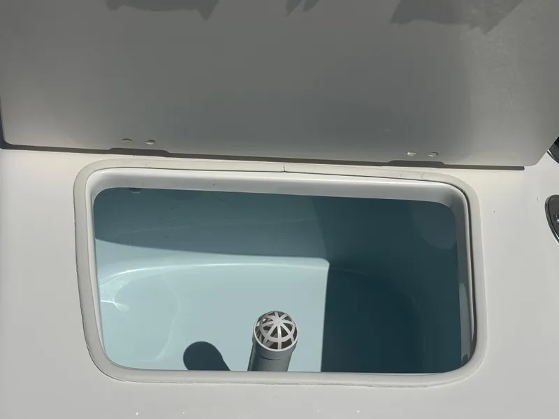Slide: The Image of 2025 Robalo R160 Center Console livewell, open lid, white interior, sunlight. - 9