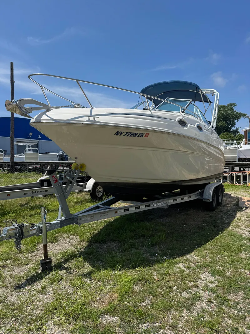 The Image of 2003 Sea Ray 240 Sundancer boat on trailer, parked on grass under clear blue sky. - 0