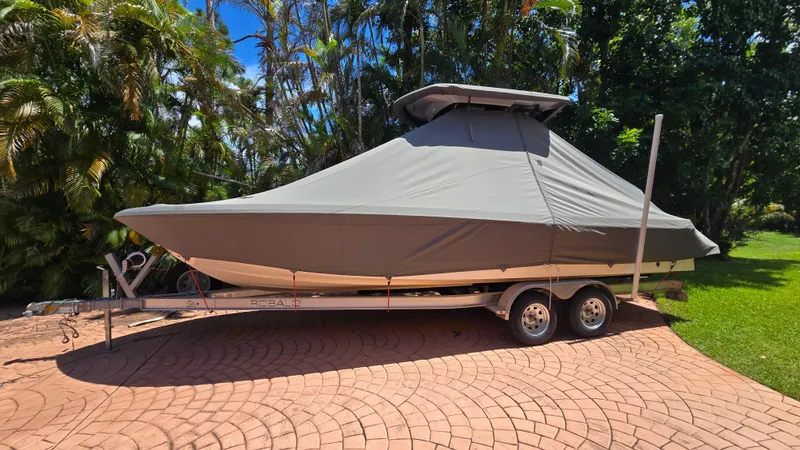 Slide: The Image of 2021 Robalo 246 Cayman boat covered on trailer, surrounded by lush greenery. - 5