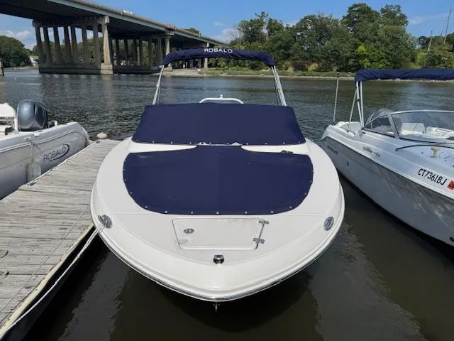 Slide: The Image of 2024 Robalo R207 Dual Console boat docked on a calm river under a clear sky. - 2