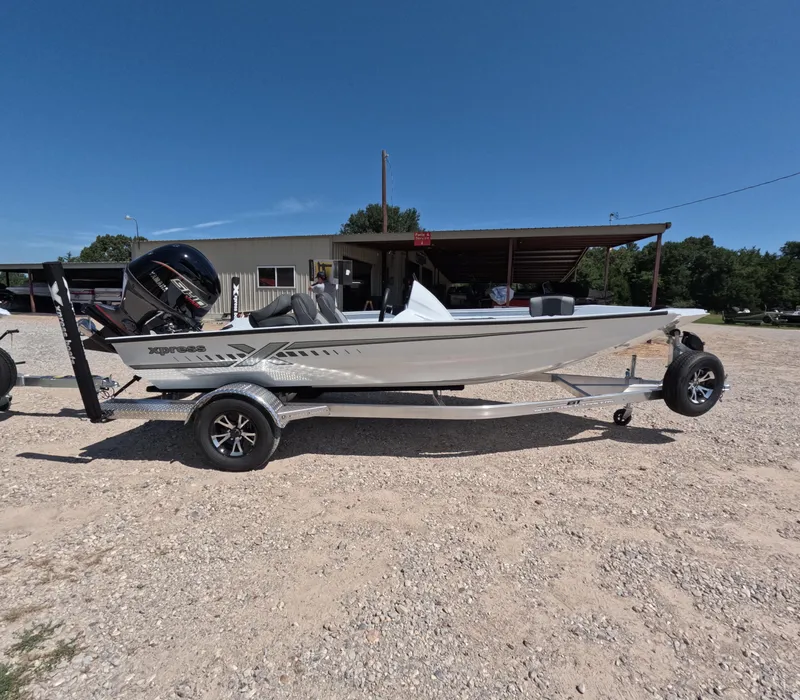 Slide: The Image of 2026 Xpress H 18 BASS boat on trailer, parked outdoors under clear blue sky. - 0