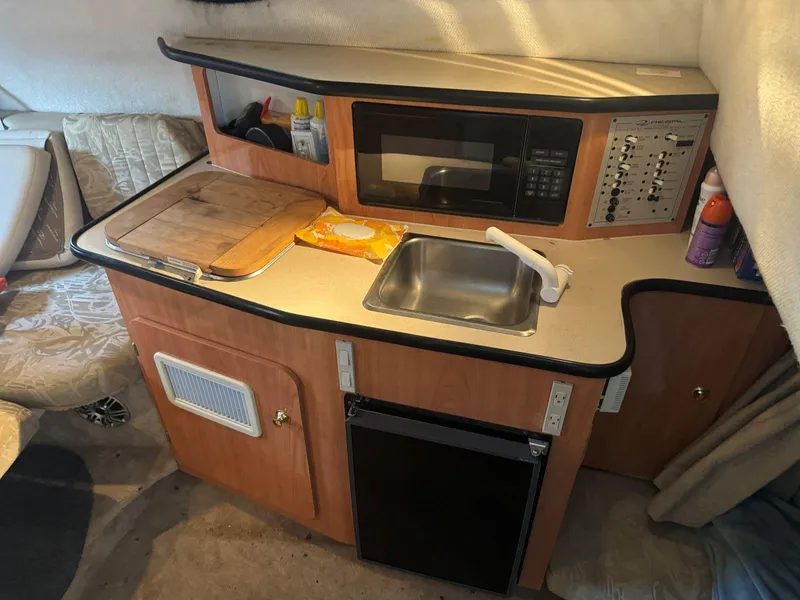 Slide: The Image of Compact kitchen area in a 2000 Regal Commodore 2460 boat, featuring a sink, microwave, and storage. - 17
