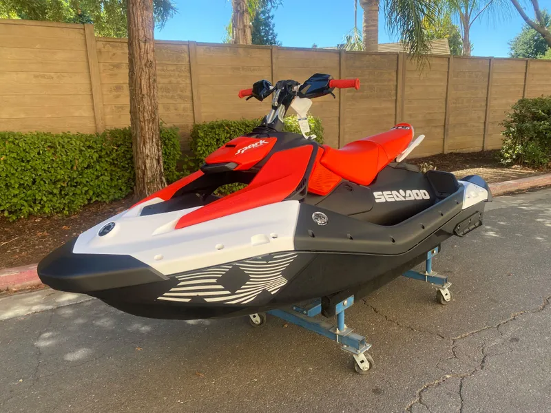 Slide: The Image of 2025 Sea-Doo SPARK TRIXX 3up jet ski in vibrant red and black, parked outdoors. - 2