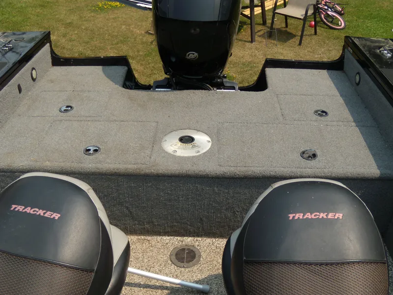 Slide: The Image of 2015 Tracker Targa V-18 WT boat interior with seating and motor, parked on grass. - 9