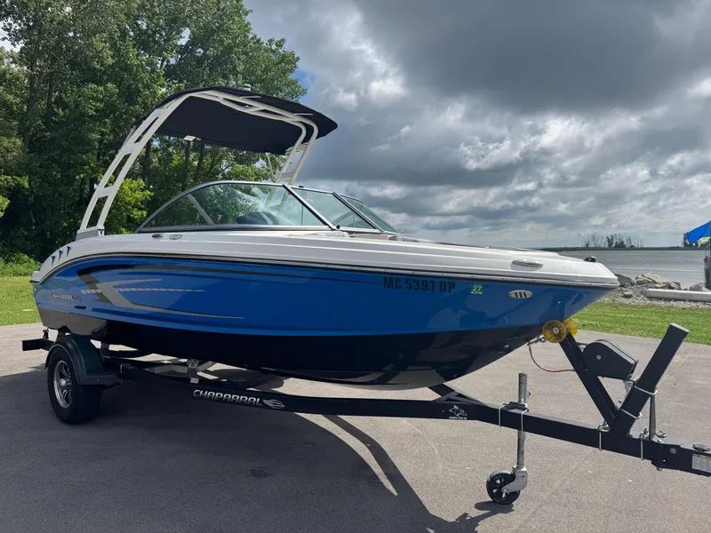 Slide: The Image of 2021 Chaparral 19 SSI Sport boat on trailer, parked near a lake under cloudy skies. - 2