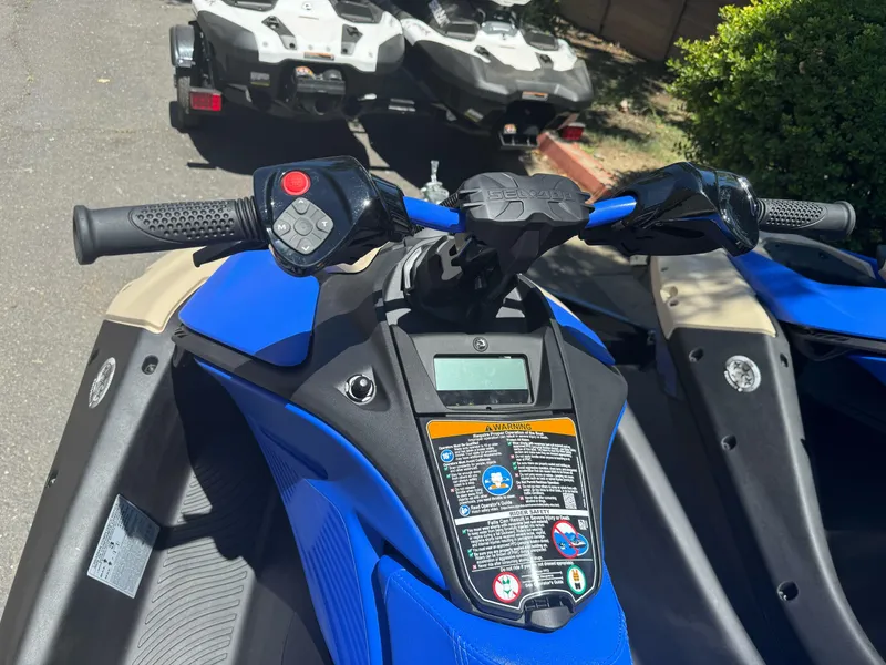 Slide: The Image of 2025 Sea-Doo SPARK TRIXX 3up, blue handlebars, control panel, parked outdoors. - 3