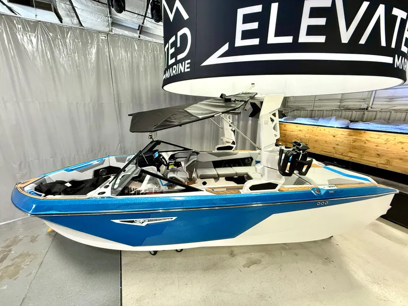 Slide: The Image of 2025 Nautique Super Air Nautique S23 boat in showroom, blue and white design, side view. - 19