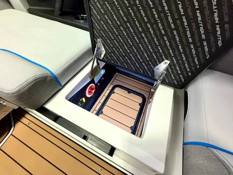Slide: The Image of 2025 Nautique Super Air Nautique S23 storage compartment with open lid and control panel. - 26